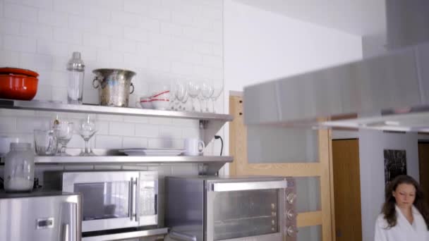 кавказка в белом халате на современной кухне с яблоком - Кадры, видео