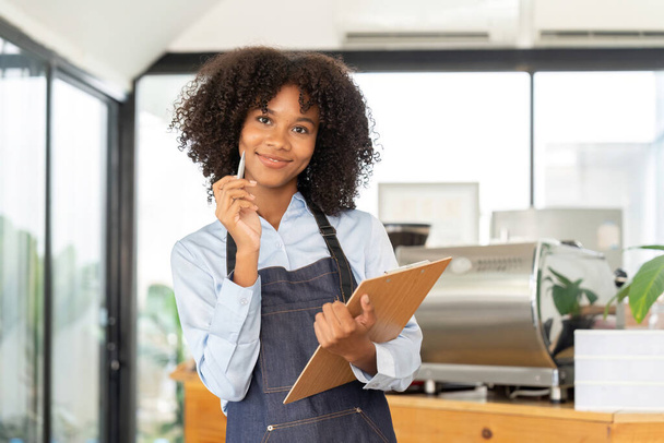 Portrait of a smiling young african american waitress wearing apron ready to take customer order. - Photo, Image