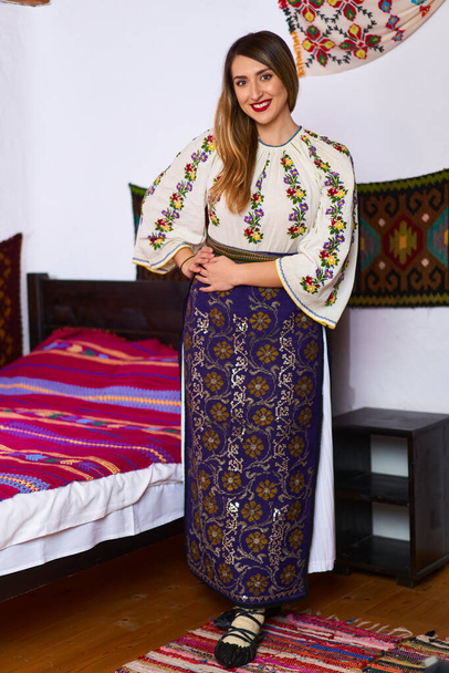 Young Romanian woman dressed up in traditional popular costume, in a traditional rural home - Zdjęcie, obraz