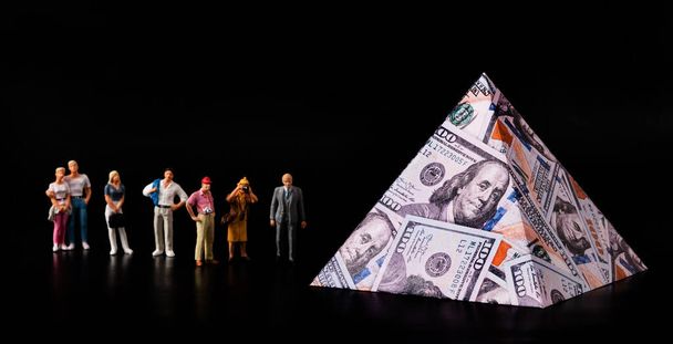 Kolejka symbolicznych postaci ludzi do piramidy z wizerunkiem banknotów o nominałach 100 dolarów amerykańskich - Zdjęcie, obraz
