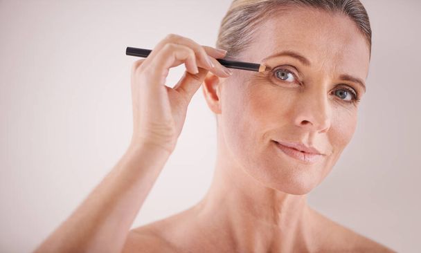Shes going for the elegant look. A cropped portrait of a beautiful mature woman applying eyeliner - Zdjęcie, obraz
