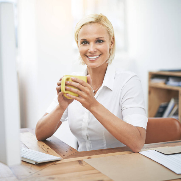 Kickstarting the workday with a strong cup of coffee. Portrait of a businesswoman drinking coffee while working at her desk - Foto, Bild