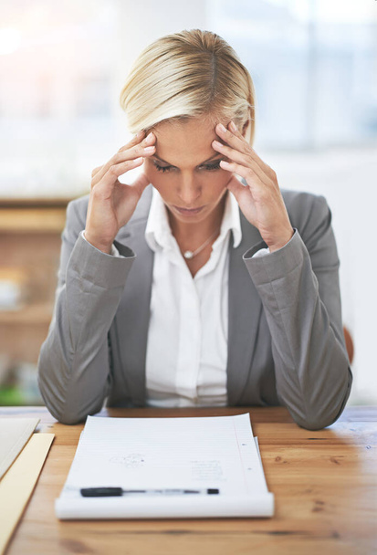Some days are just one big headache...a businesswoman sitting at her desk looking stressed - Valokuva, kuva