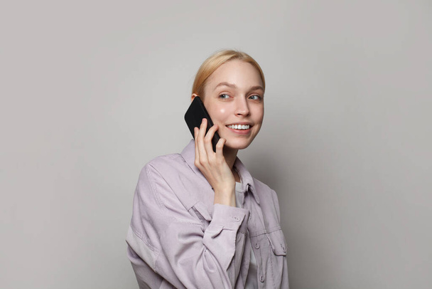 Étudiant souriant jeune femme portant des vêtements décontractés parlant au téléphone sur fond de bannière murale studio blanc - Photo, image