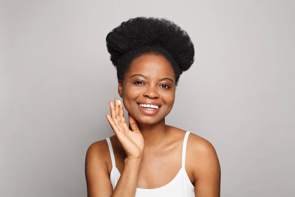 Счастливая молодая женщина показывает увлажняющий крем для кожи лица. Здоровая модель спа-салона с чистой кожей на белой стене студии - Фото, изображение