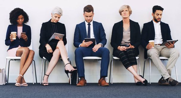 Tablet, phone and recruitment people row with young, senior and corporate candidates in work lobby. Social media, email and online communication of group in chair queue at professional job interview - Foto, Imagem