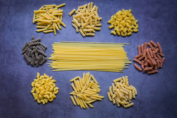 Raw pasta various kinds of uncooked pasta macaroni spaghetti and noodles on wooden, Italian food culinary concept, Collection of different raw pasta on cooking table for cooking food - top view - Photo, Image