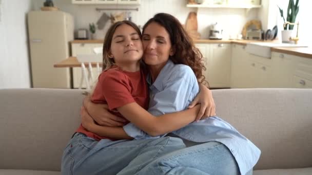 Friendly Caucasian woman and teenage girl hugging rejoice meeting after long separation. Happy mother and daughter schoolgirl in casual clothes are sits on sofa smiling and cuddle to each other - Footage, Video