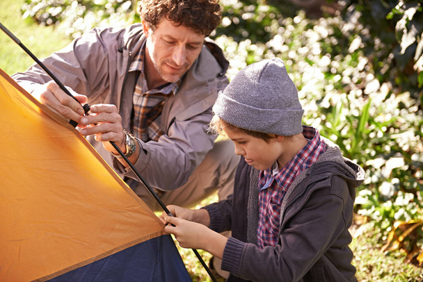 Aventures en plein air avec papa. Un petit garçon mignon aidant son père à planter une tente à l'extérieur - Photo, image