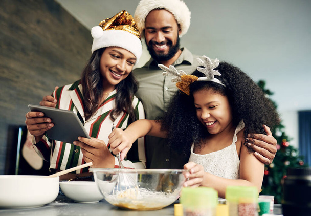 Noël, la famille et la cuisson avec une fille et les parents mélangeant la pâte tout en utilisant une recette de tablette en ligne ensemble. Nourriture, enfants et cuisine avec une mère, père et fille apprenant à cuisiner. - Photo, image