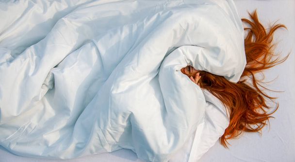 seksikäs punapää nainen sängyssä, kasvot lähes tyynyn alla, kurkistaa ulos, aurinkoisena kesäaamuna, kopioi tilaa - Valokuva, kuva