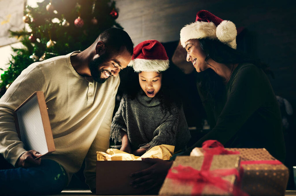Счастливый семейный, приятный или неожиданный подарок в ночном доме или домашней гостиной в торжественном случае, празднике или отпуске. Улыбнись, счастливый или шокированный ребенок, мама или отец Рождества и подарить. - Фото, изображение