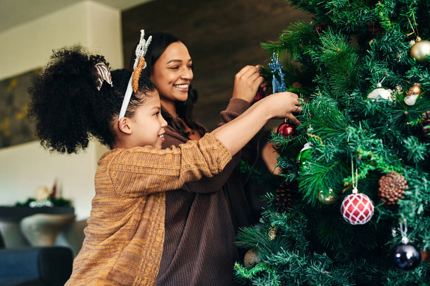 Moeder, meisje en band met kerstboom decoratie in familie huis of huis voor viering evenement, feestelijke vakantie of vakantie. Glimlach, vrolijke of kerst vrouw en kind opknoping lichten, ballen of decor. - Foto, afbeelding