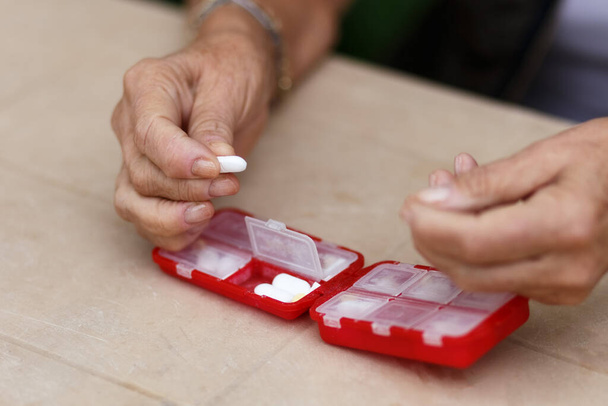 Seniorenhanden nemen pillen uit de doos. Gezondheidszorg en ouderdomsconcept met geneesmiddelen. Medicamenten op tafel. close-up - Foto, afbeelding