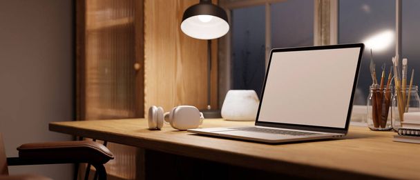 Hangulatos skandináv otthoni munkaterület laptop üres képernyő mockup, fény asztali lámpa, fejhallgató, festőeszközök fa asztalon. Egy közeli kép. 3D render, 3D illusztráció - Fotó, kép