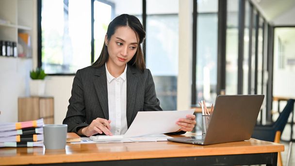 Profesional y exitosa empresaria asiática milenaria centrada en su tarea en el papeleo, trabajando en su escritorio en la oficina. - Foto, Imagen