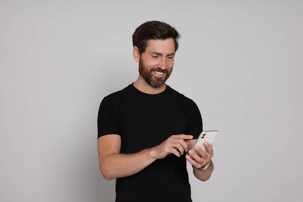 Happy man with smartphone on light background - Φωτογραφία, εικόνα
