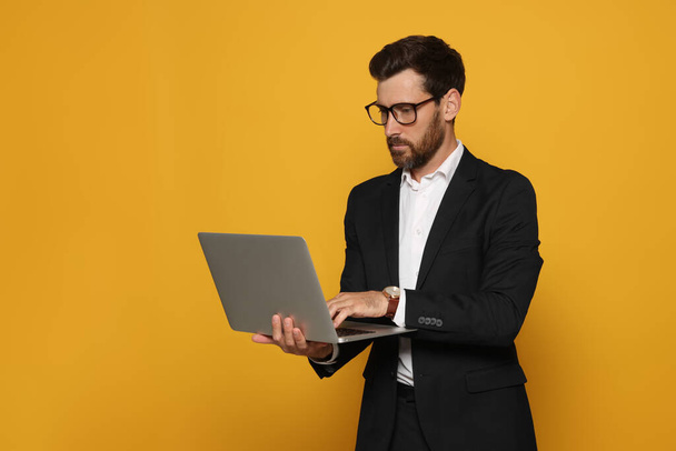Bearded man with glasses working on laptop against orange background - Photo, image