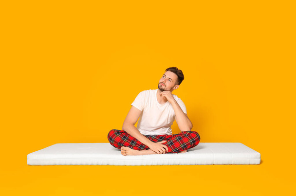 Man sitting on soft mattress against orange background - Fotografie, Obrázek
