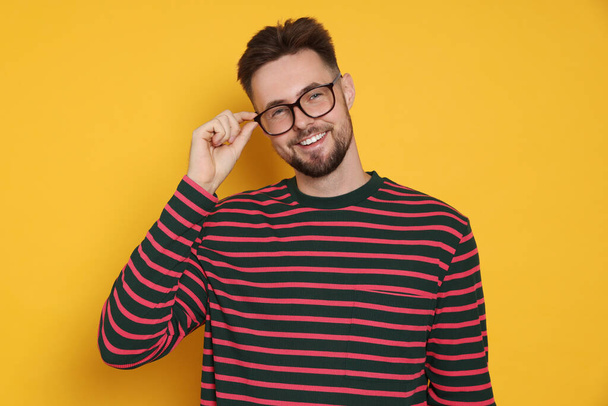 Handsome man in striped sweatshirt and eyeglasses on yellow background - Φωτογραφία, εικόνα