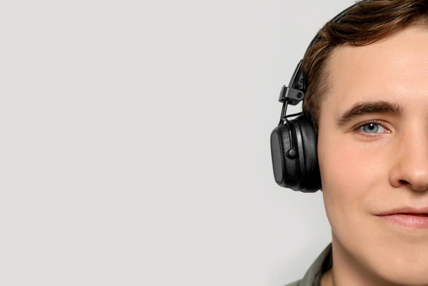 Handsome young man with headphones on light grey background, closeup. Space for text - Фото, изображение