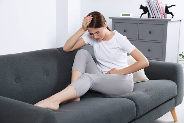 Young woman suffering from cystitis on sofa at home - Φωτογραφία, εικόνα