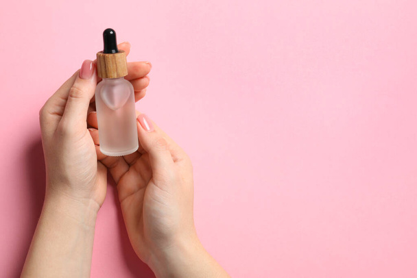 Woman holding bottle with serum on pink background, top view. Space for text - Fotó, kép