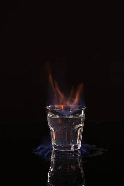 Flaming vodka in shot glass on black background - Fotoğraf, Görsel