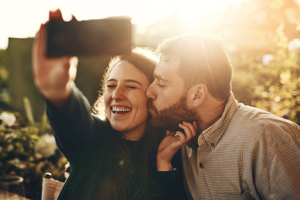 Couple, kiss and phone for happy selfie, love or relationship bonding moments together in nature. Man and woman with smile for loving romance, travel or vacation photo with smartphone in the outdoors. - Foto, imagen
