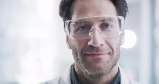 Ciencia, laboratorio y retrato de hombre con gafas de seguridad para protección ppe en pruebas médicas, investigación y análisis. Innovación sanitaria, visión y rostro del científico masculino con sonrisa en el laboratorio. - Metraje, vídeo