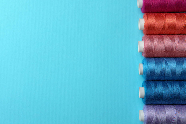 Set of different colorful sewing threads on light blue background, flat lay. Space for text - Foto, Bild
