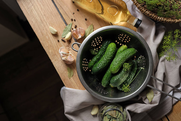 Fresh cucumbers in colander and other ingredients prepared for canning on wooden table, flat lay. Space for text - 写真・画像
