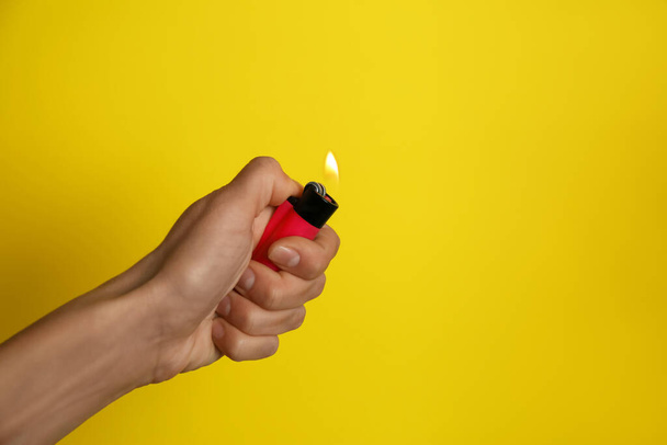 Woman holding pink lighter on yellow background, closeup. Space for text - Fotó, kép