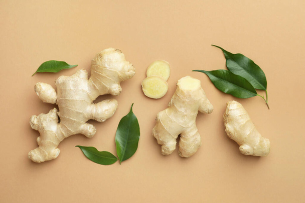 Fresh ginger with green leaves on light pale brown background, flat lay - Фото, изображение