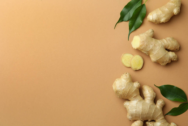 Fresh ginger with green leaves on light pale brown background, flat lay. Space for text - Foto, immagini