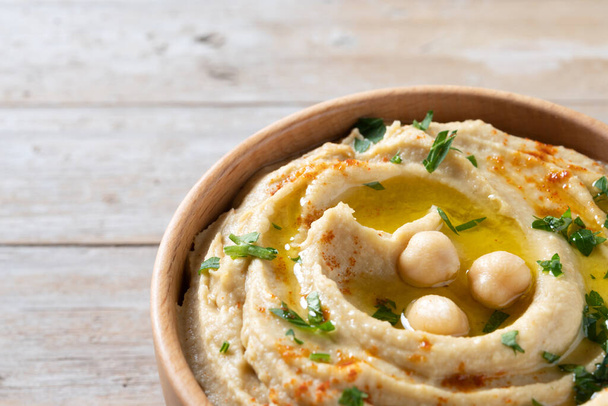 Chickpea hummus in a wooden bowl garnished with parsley, paprika and olive oil on wooden table. Copy space - Φωτογραφία, εικόνα