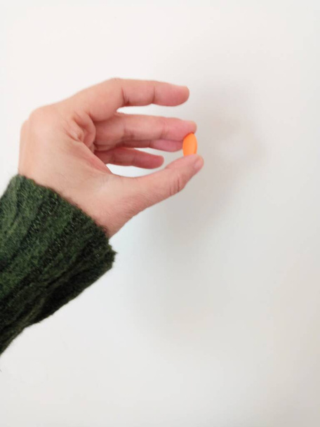 Die Frau hält die Pille zwischen ihren beiden Fingern. Orangefarbene Pille. - Foto, Bild