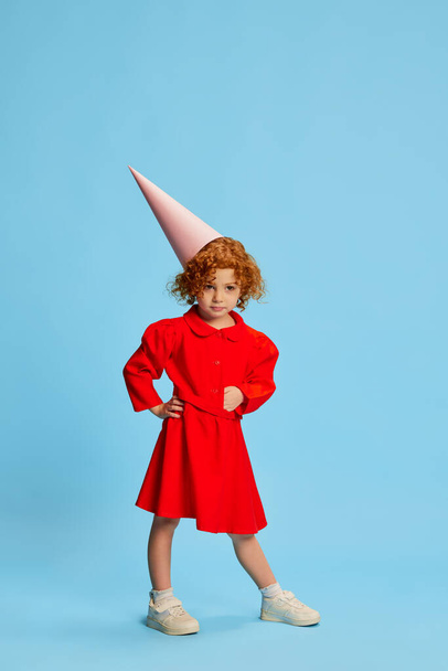 Cute little girl, child with curly red hair posing in costume of a fairy isolated over blue background. Birthday. Concept of childhood, emotions, lifestyle, fashion, happiness. Copy space for ad - Fotografie, Obrázek