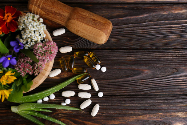 Mortar with fresh herbs, flowers and pills on wooden table, flat lay. Space for text - Foto, immagini