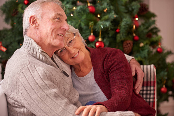 Karácsony, szerelem és idős pár ölelés kanapén otthon, szeretet és kötődés. Románc, karácsony ünnep és boldog idős, nyugdíjas nő és férfi ölelkeznek a kanapén élvezve minőségi időt együtt a házban. - Fotó, kép