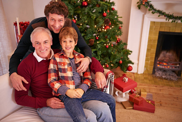 Portrait of a grandfather, father and child at a christmas event relaxing on sofa together. Happy, smile and senior man in retirement sitting with dad and boy kid at festive xmas celebration at home - Foto, immagini
