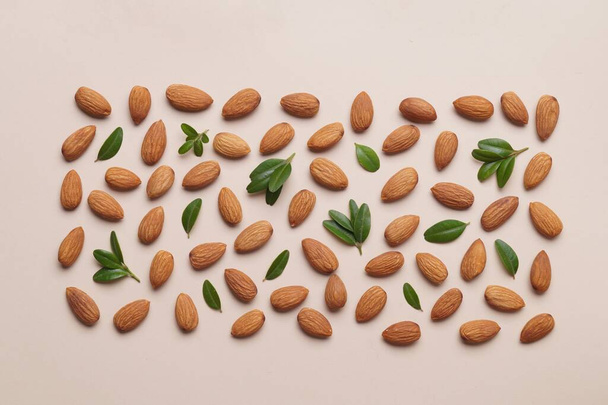 Delicious almonds and fresh leaves on beige background, flat lay - Fotoğraf, Görsel