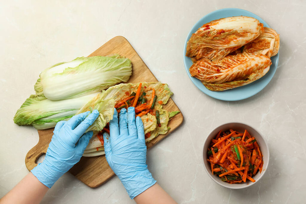 Woman preparing spicy cabbage kimchi at beige marble table, top view - Valokuva, kuva