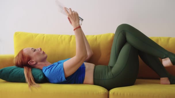 Adult woman lying on the couch and reading book. Mid shot - Footage, Video