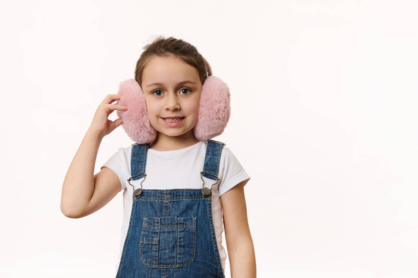 Happy child, lovely baby girl wearing cute pink winter earmuffs - plush headphones, ccarefully smiling looking at camera, isolated over white background. Защищай уши от холода. Копирование текста - Фото, изображение