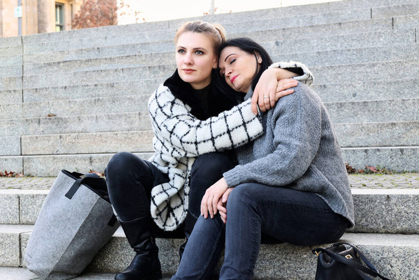 two women sitting outdoors on steps and hugging - Foto, Imagem