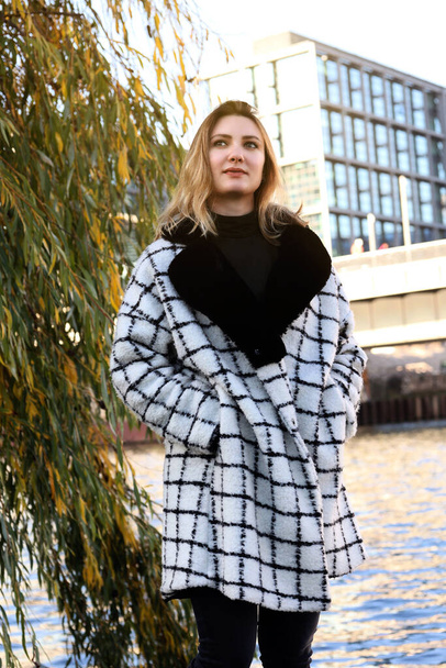 young woman in a coat walking along a river in the city - Foto, afbeelding