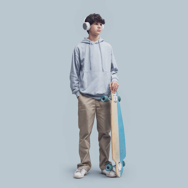 Крутий підліток позує зі скейтбордом, ізольований на сірому фоні
 - Фото, зображення