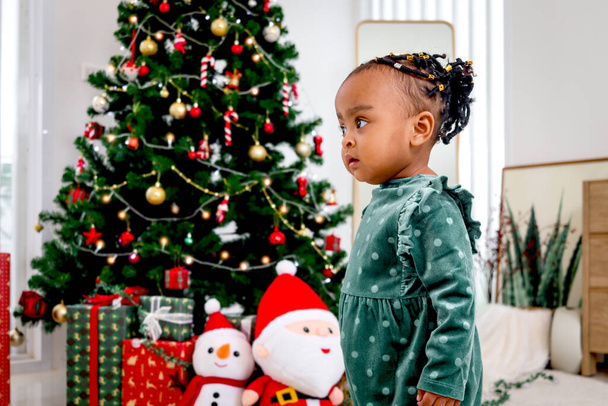 Portrait of adorable African American little girl child standing in living room with many gift boxes presents under Christmas tree, kid celebrating happy Christmas winter holiday - Photo, Image