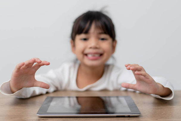 Aziatisch klein schattig meisje aanraken van de digitale tablet scherm op de tafel  - Foto, afbeelding